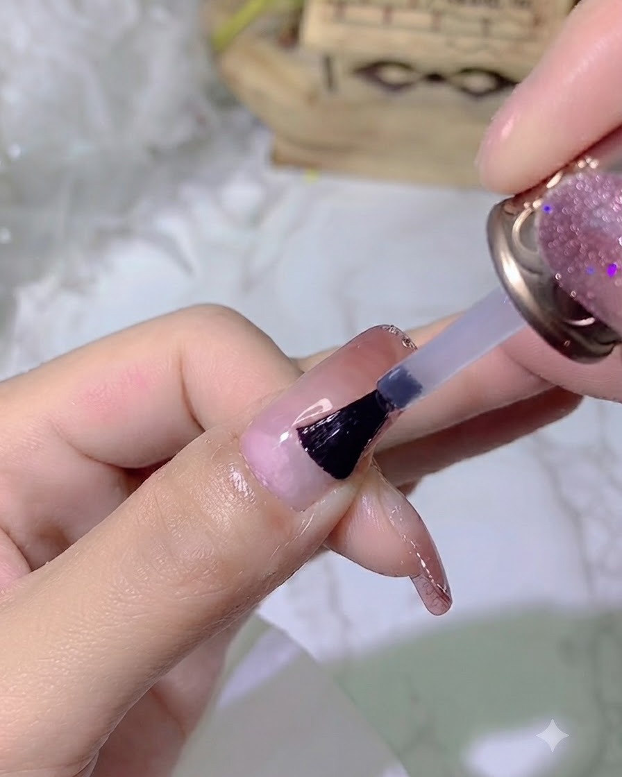 Un pinceau appliquant un top coat transparent et brillant sur un onglet manucuré.