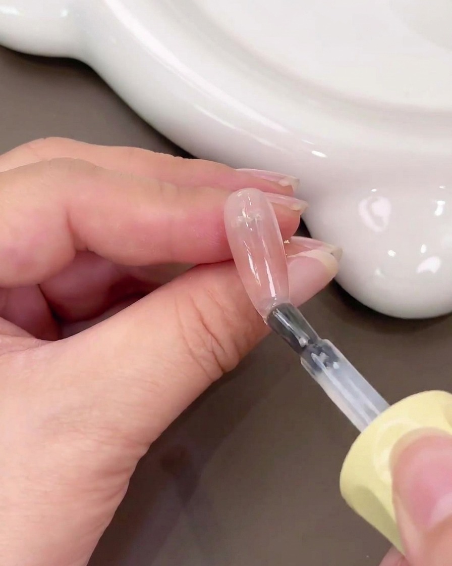 Un pinceau appliquant du gel de base transparent sur un ongle doté dun dégradé blush rose.