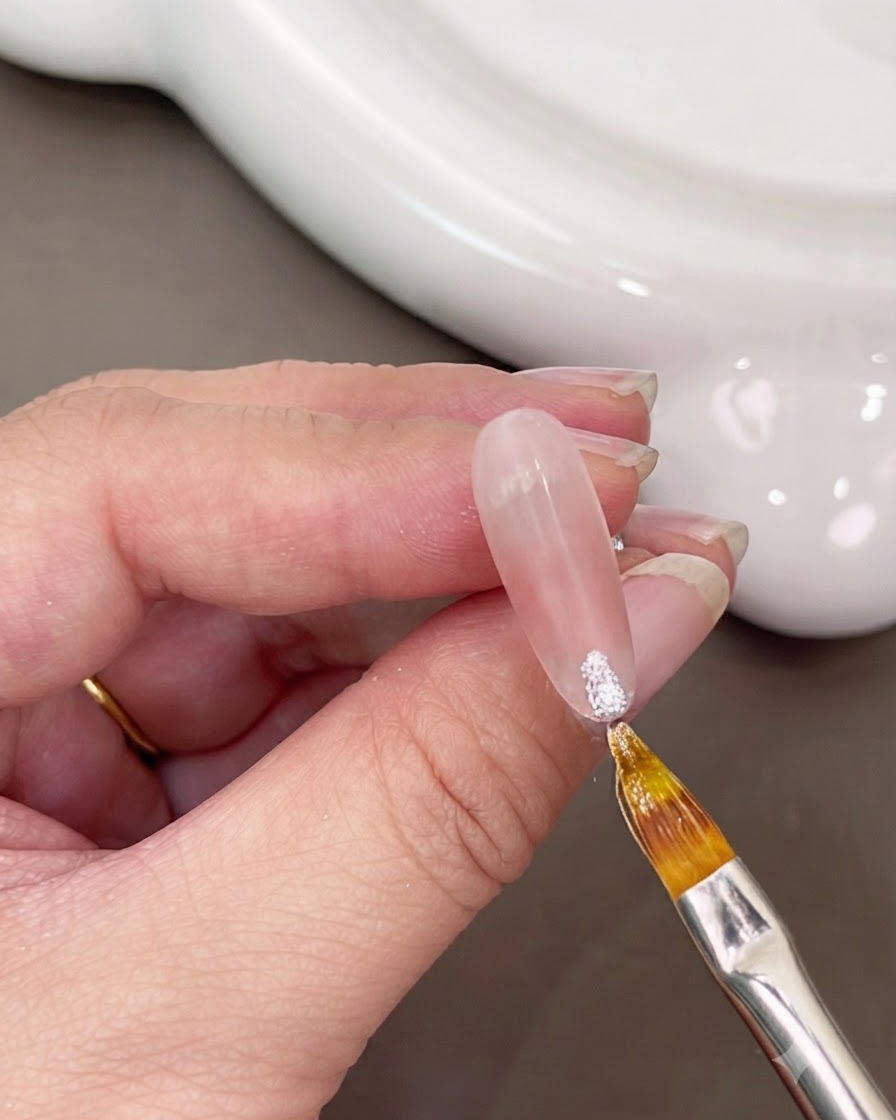 Un pinceau fin appliquant du gel blanc scintillant sur le bout dun ongle.