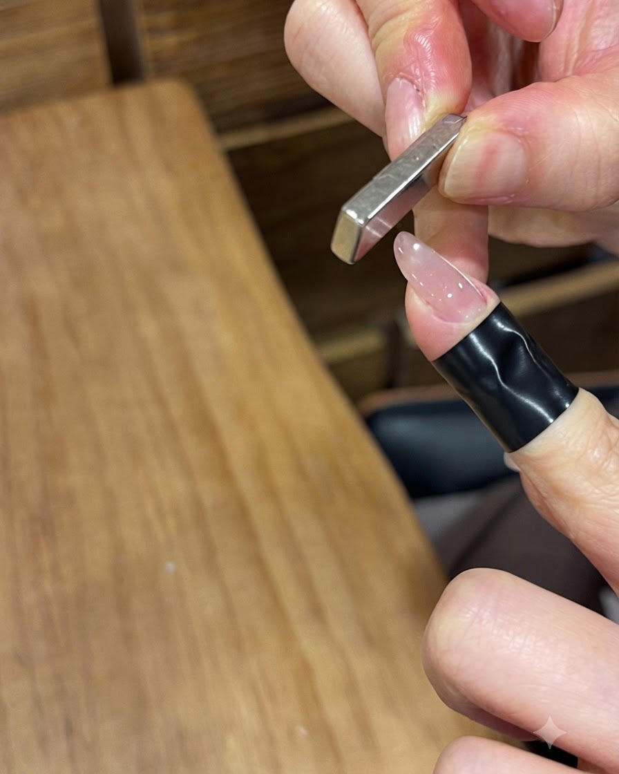 Un aimant rectangulaire plat tenu verticalement près dun ongle verni brillant pour repousser les particules magnétiques.