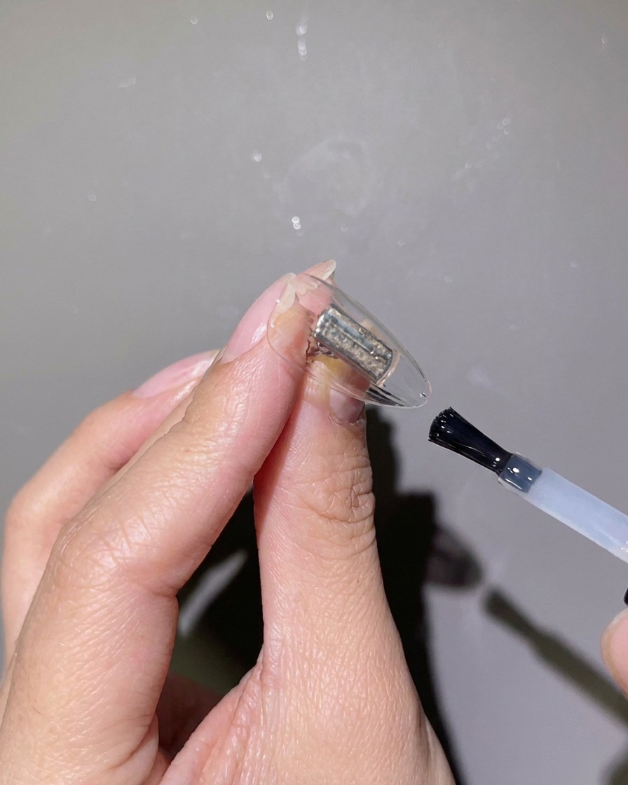 Gros plan dun pinceau appliquant un gel de renforcement transparent sur une capsule dongle claire.