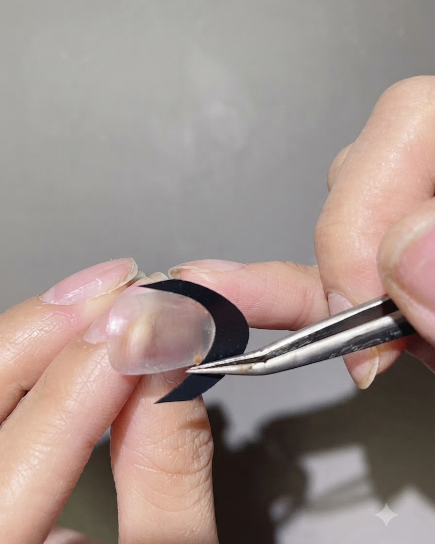 Une paire de tweezers plaquant un guide autocollant noir incurvé pour French sur la surface dun ongle transparent.