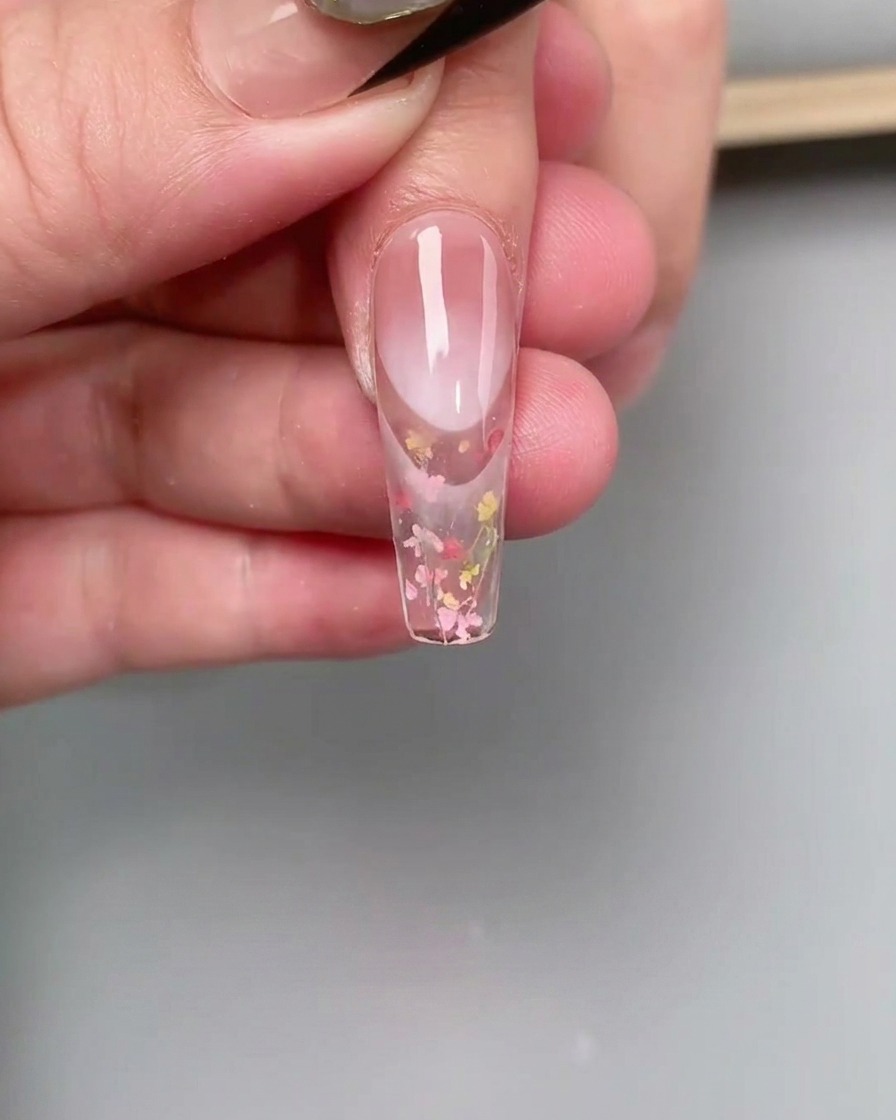 Un pinceau fin estompant du gel de couleur rose au niveau de la cuticule pour créer un effet ombré.