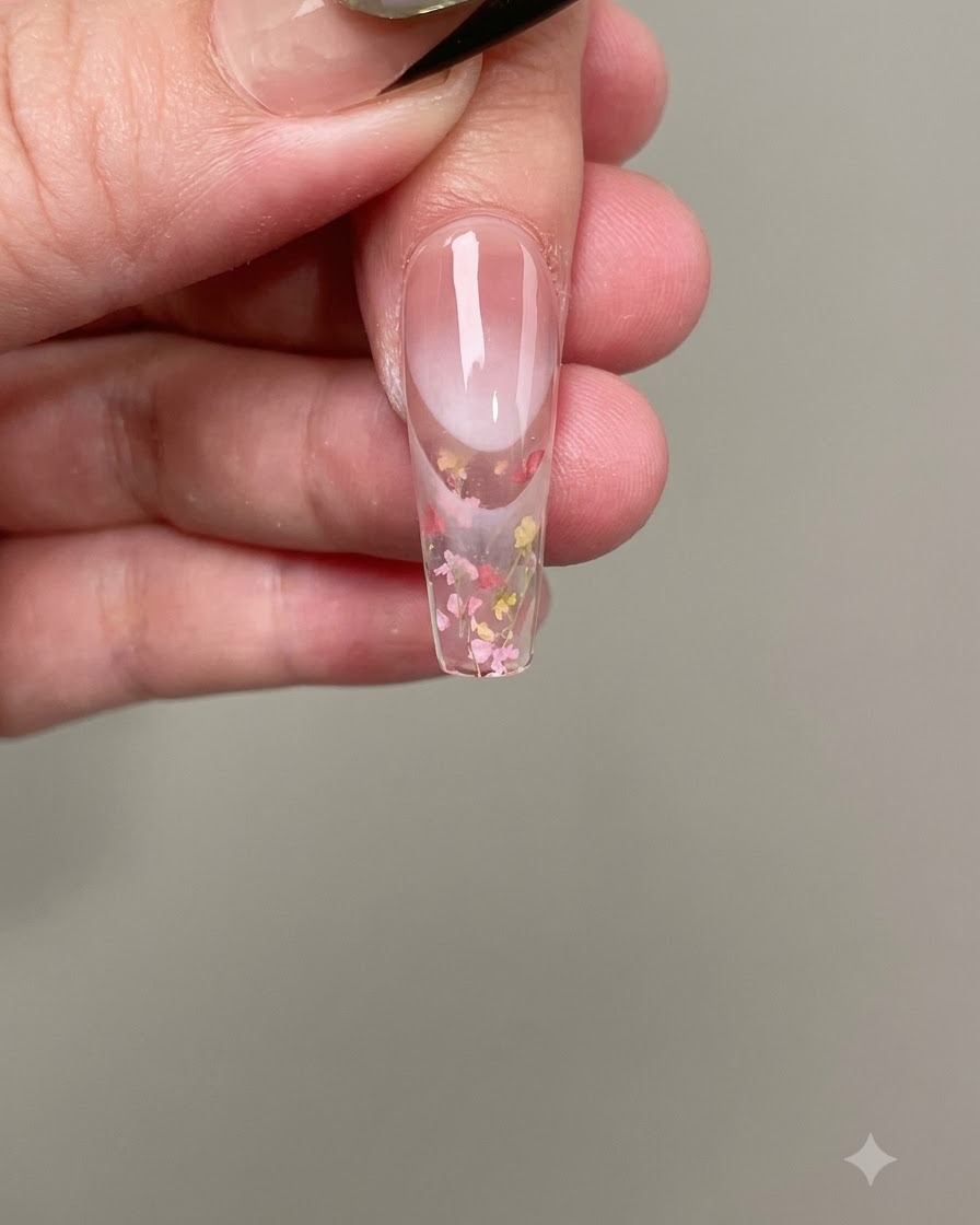 Une pince à épiler plaçant de minuscules fleurs séchées roses et jaunes sur le gel à ongles humide.