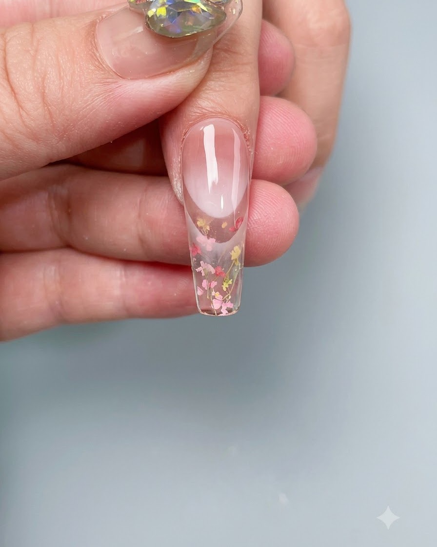 Un ongle avec des fleurs séchées intégrées catalysant à lintérieur dune lampe à ongles professionnelle UV/LED.