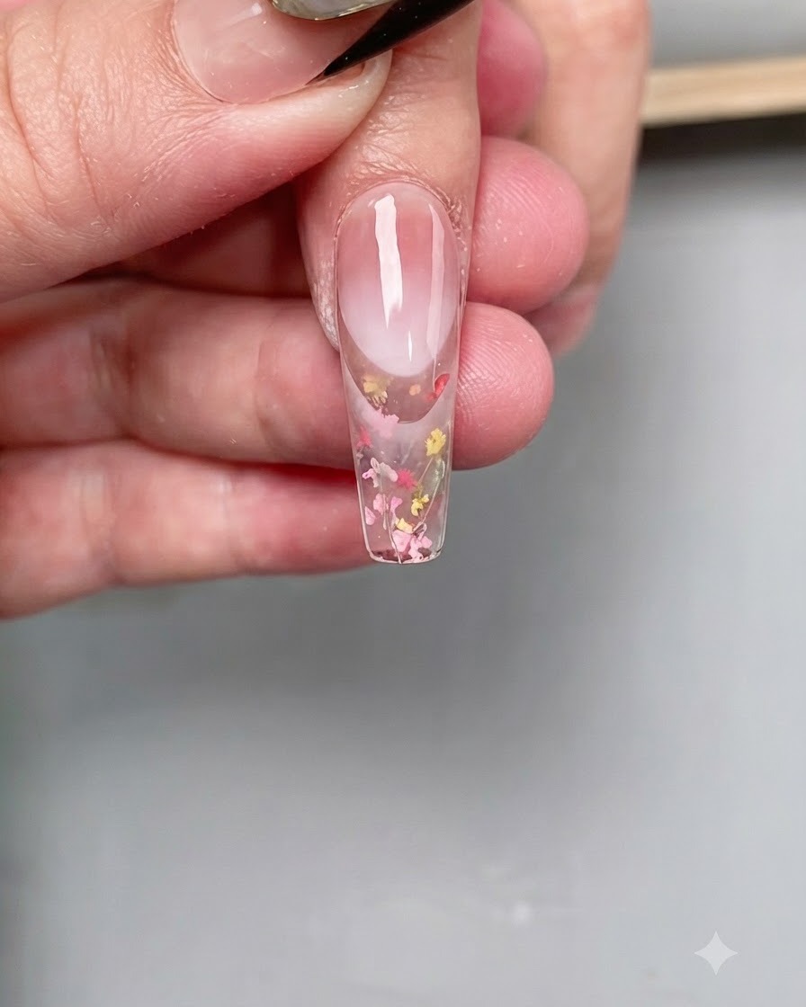Un pinceau de nail art fin appliquant un top coat diamant transparent précisément sur le bout dun ongle long en forme de cercueil.