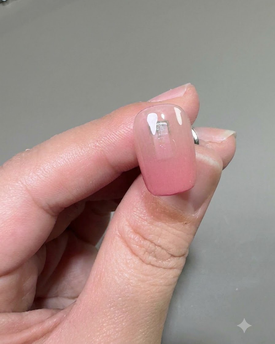 Gros plan dun ongle montrant une couche transparente de gel de renforcement appliquée sur la base dégradée rose.