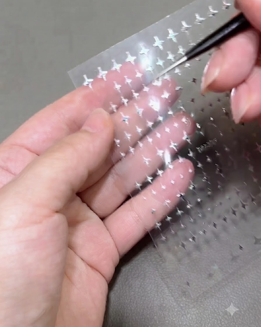 Gros plan dun outil de détail soulevant un minuscule autocollant étoile argenté dune feuille transparente tenue au-dessus de la paume dune personne.