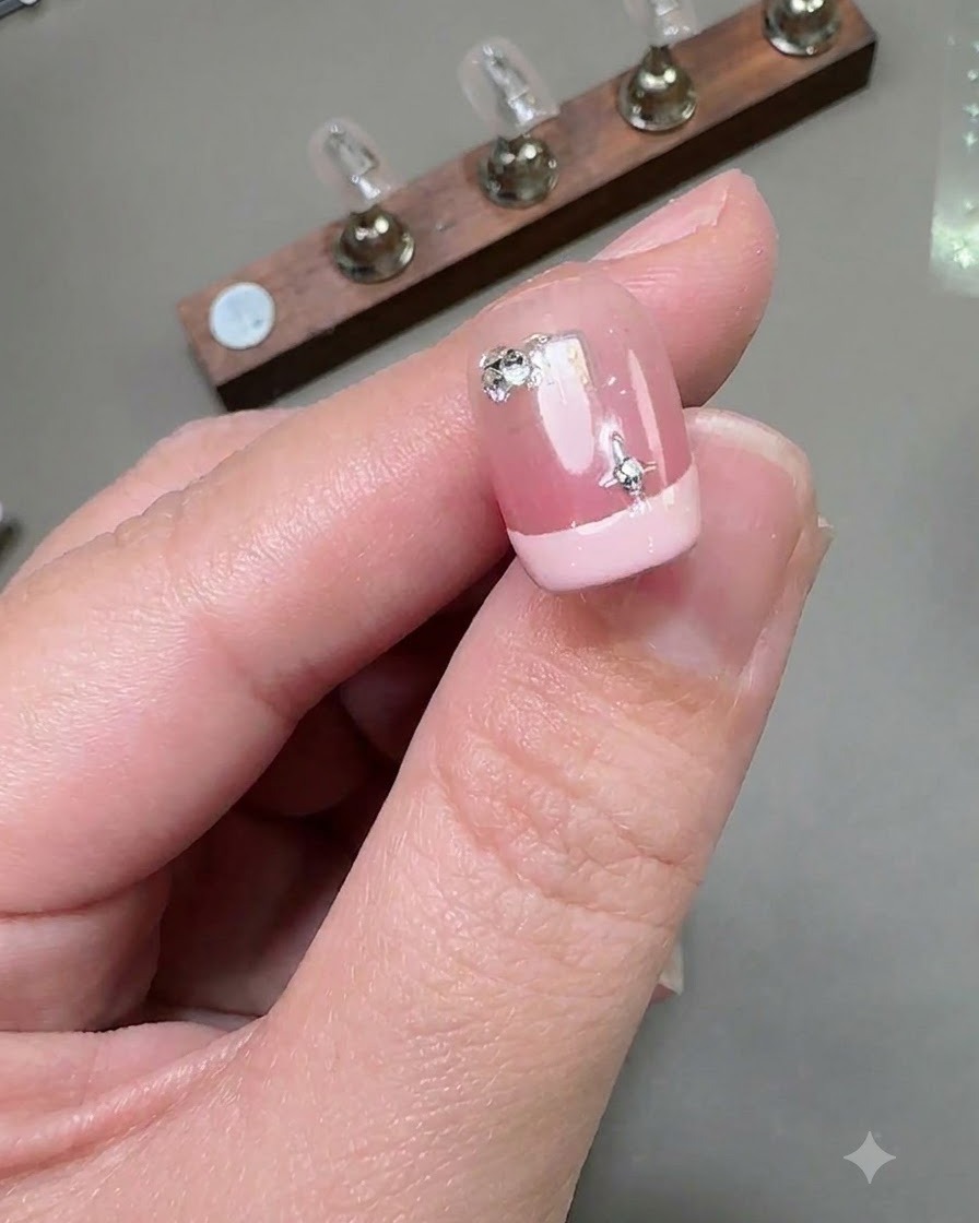 Vue rapprochée dun ongle court de manucure française comportant un autocollant étoile argenté et un petit diamant rond fixé près de la zone des cuticules.
