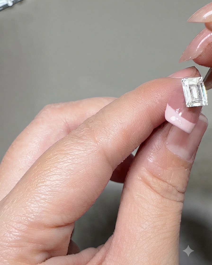 Une paire de pinces plaçant un grand cristal rectangulaire au centre dun ongle manucuré à la française.