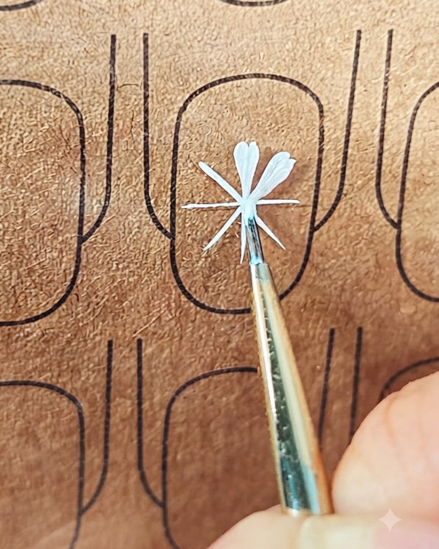 Un pinceau de nail art fin déposant du gel blanc pour former un deuxième pétale sur un présentoir dentraînement.