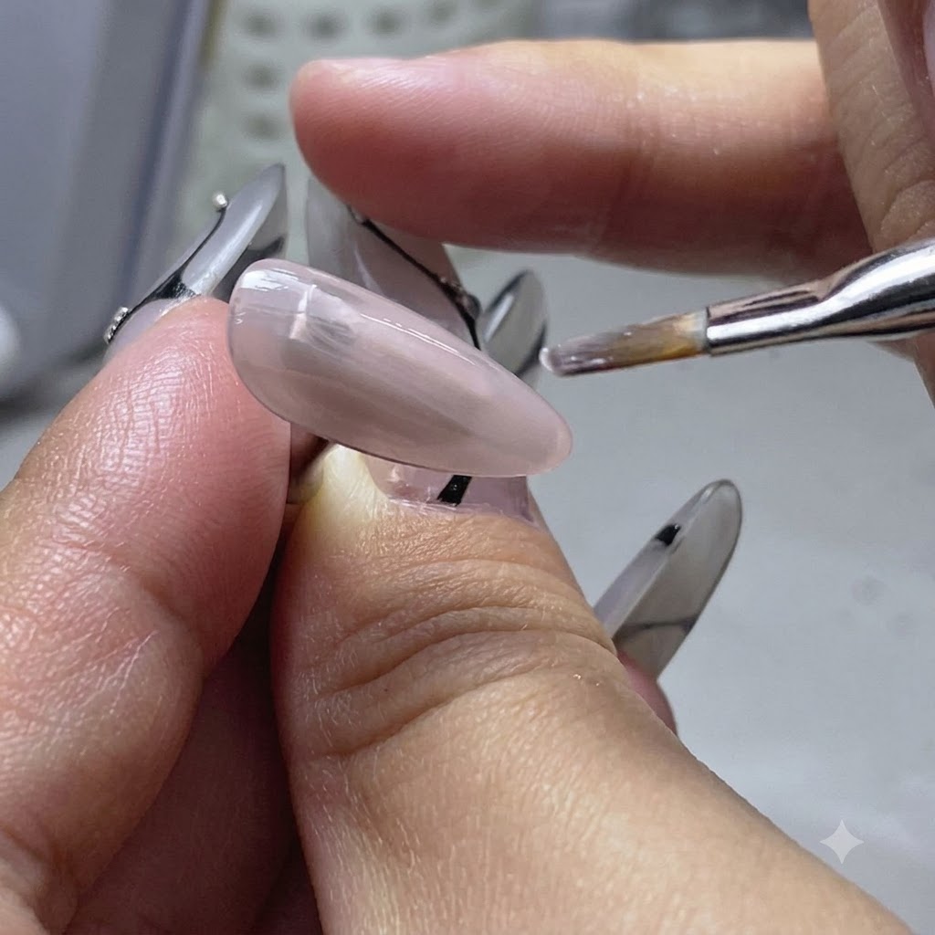 Un pinceau plat appliquant une fine couche de gel de base nude sur un ongle dentraînement.