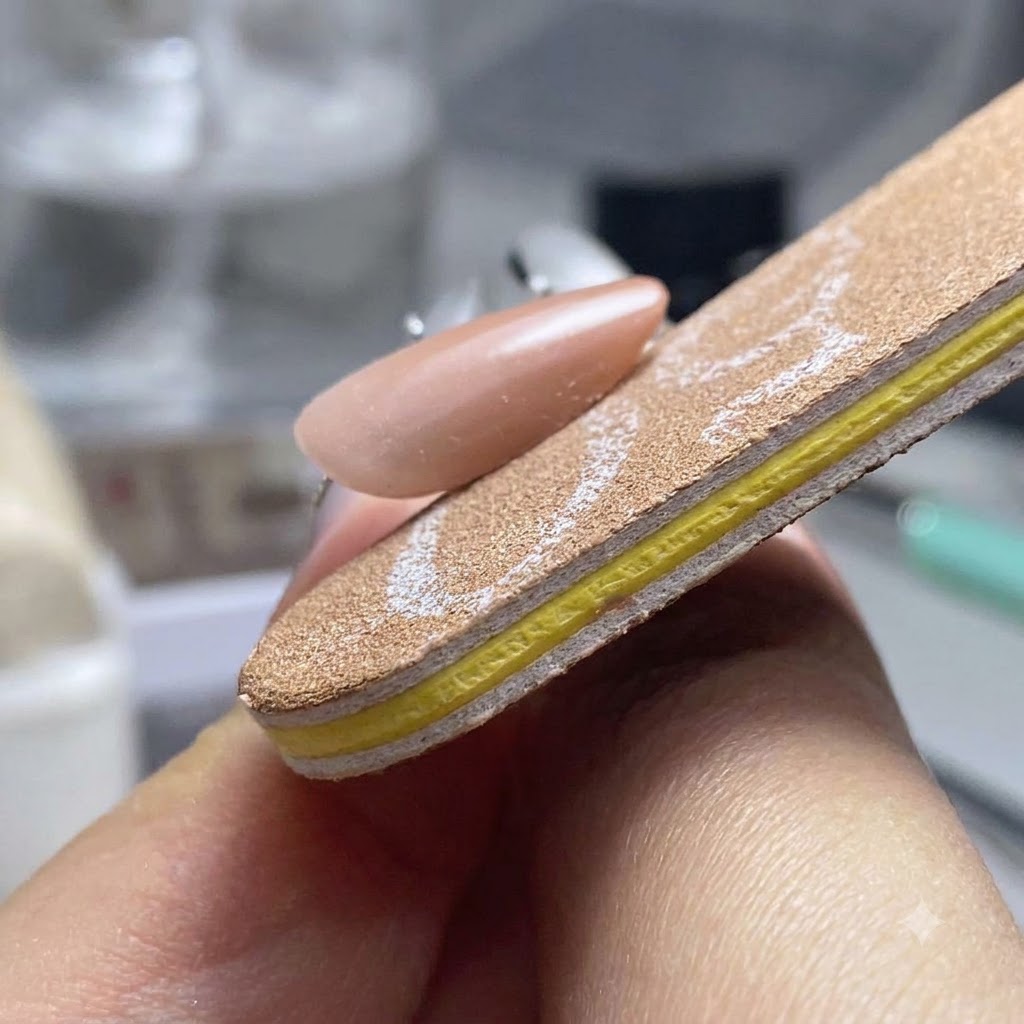 Un bloc polisseur façonnant et lissant les trois côtés dun ongle en gel terminé.