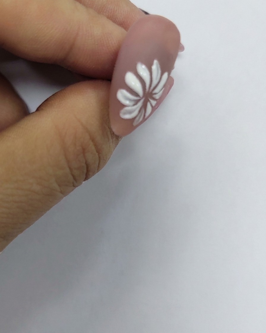 Une marguerite blanche peinte sur un ongle avec un minuscule point jaune placé précisément en son centre.