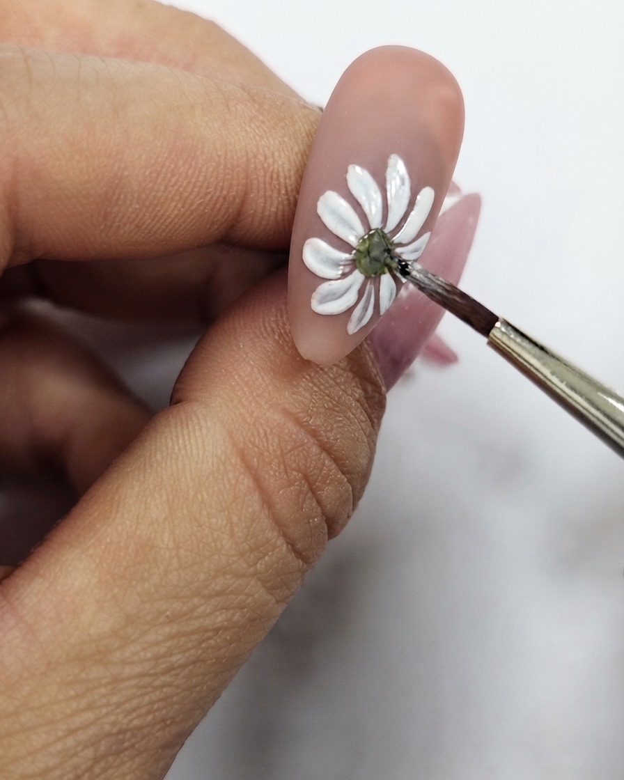 Gros plan dun pinceau fin affinant le point central jaune du nail art marguerite blanche.