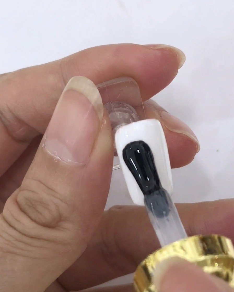Un pinceau appliquant une couche transparente de blooming gel sur une surface dongle peinte en blanc.