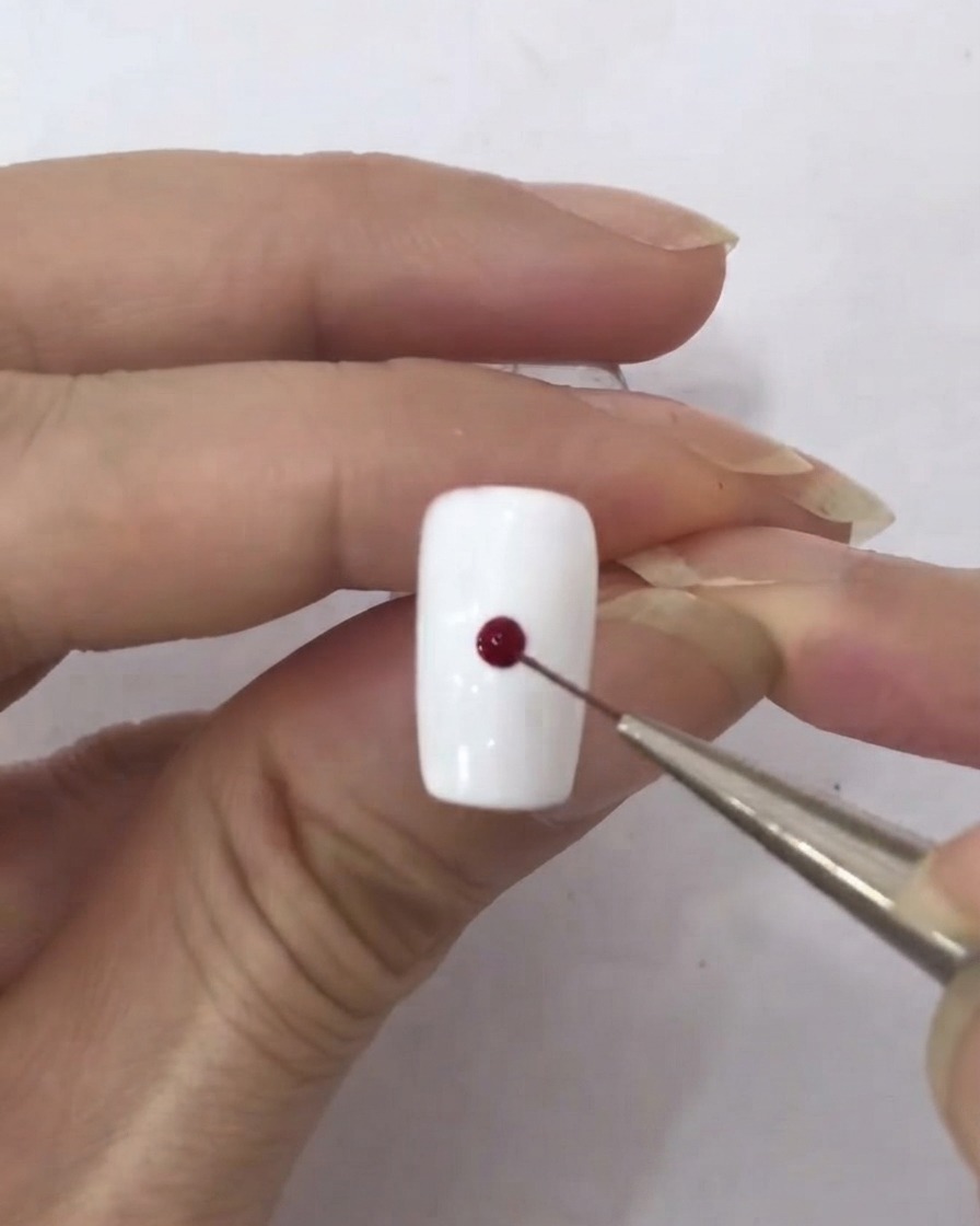 Un pinceau fin prélevant une minuscule goutte de vernis gel rouge foncé.
