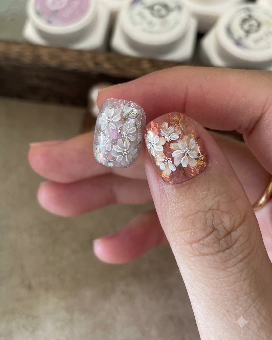 Un pinceau liner fin dessinant les contours de fleurs blanches à cinq pétales sur un ongle décoré.
