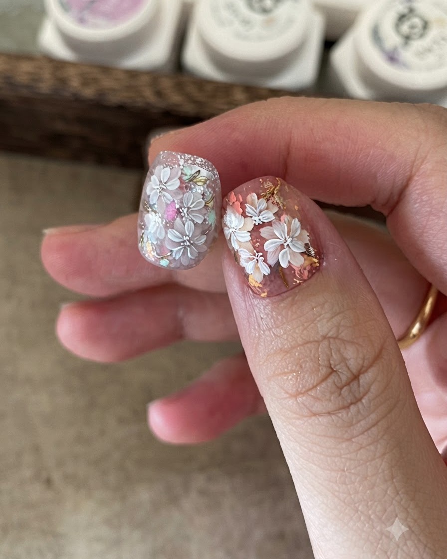 Gros plan dune prothésiste ongulaire utilisant une petite éponge pour appliquer du gel coloré au centre du nail art floral blanc.