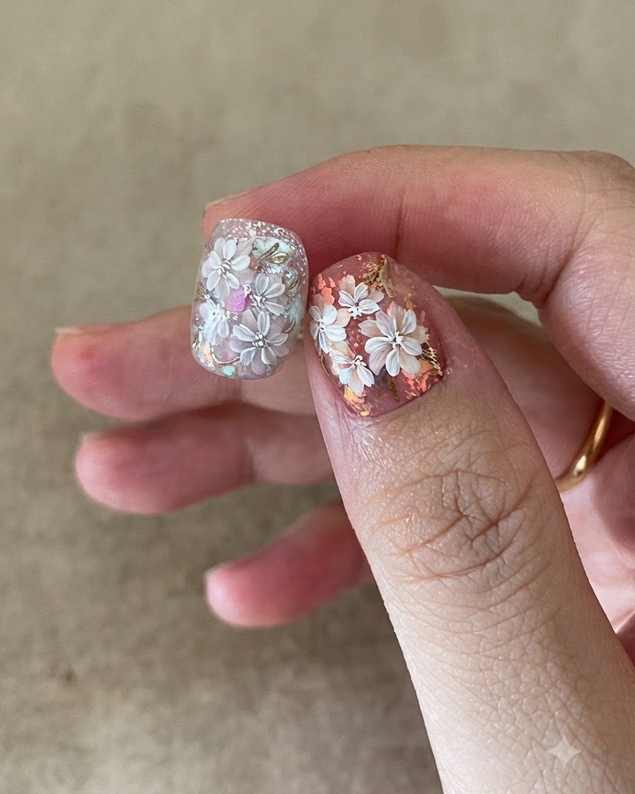 Un pinceau à ongle appliquant un top coat transparent sur un nail art complexe composé de fleurs et de foil doré.