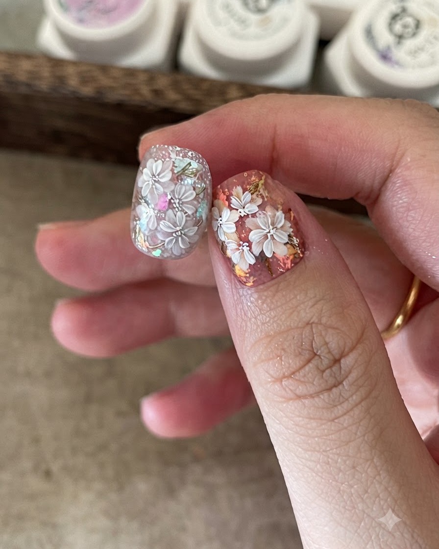 Un pinceau fin pour nail art ajoutant des pétales blancs détaillés par-dessus un design floral déjà peint.