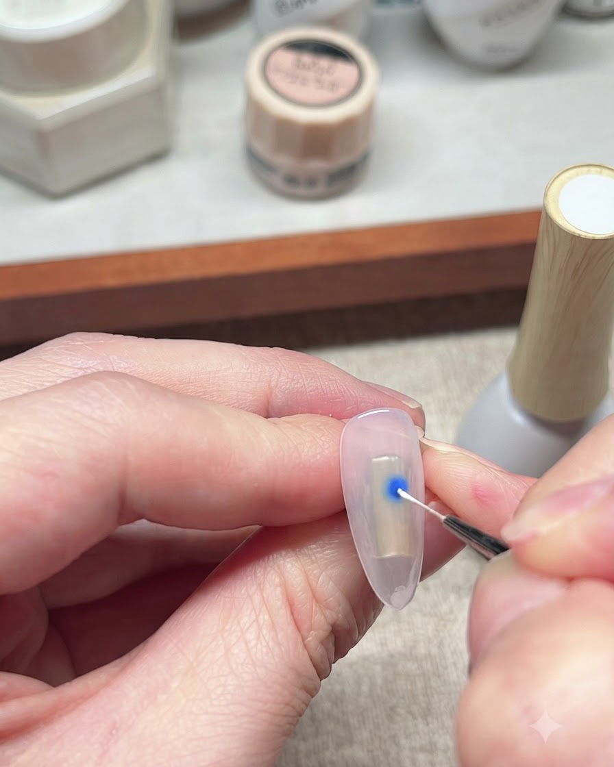 Un pinceau liner fin interagissant avec un point de vernis gel bleu sur un ongle pour lancer leffet de diffusion.