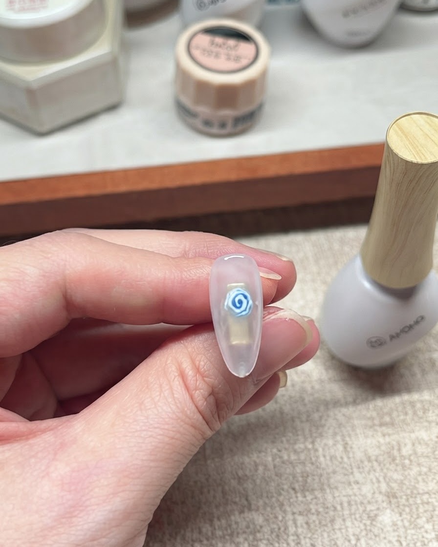 Gros plan dun nail art de rose bleue en gel terminé posé à côté dun flacon de produit blanc.