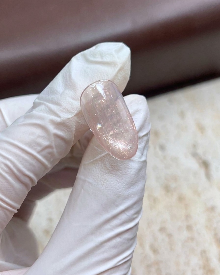 Une main gantée tenant un bâtonnet aimanté au-dessus dun ongle en gel œil de chat scintillant pour créer un effet perle.