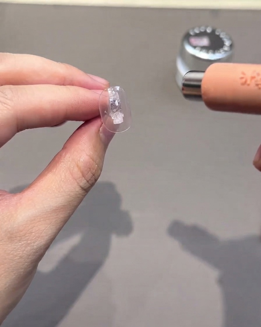 Un faux ongle transparent en cours de catalysation sous une petite lampe UV/LED portable.