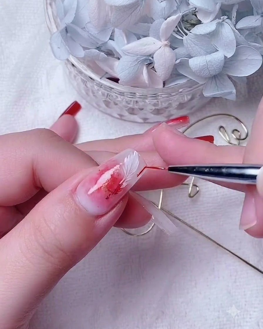 Gros plan dune prothésiste ongulaire utilisant un pinceau de détail fin pour estomper le gel rouge sur un ongle à base blanc laiteux.