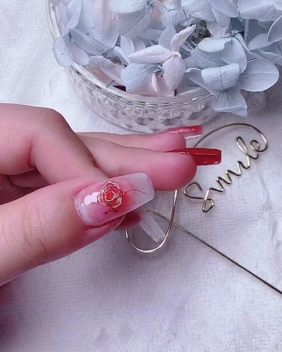 Gros plan dun ongle de pouce décoré présentant une rose en fil doré et de petits fils daccentuation le long du bord.