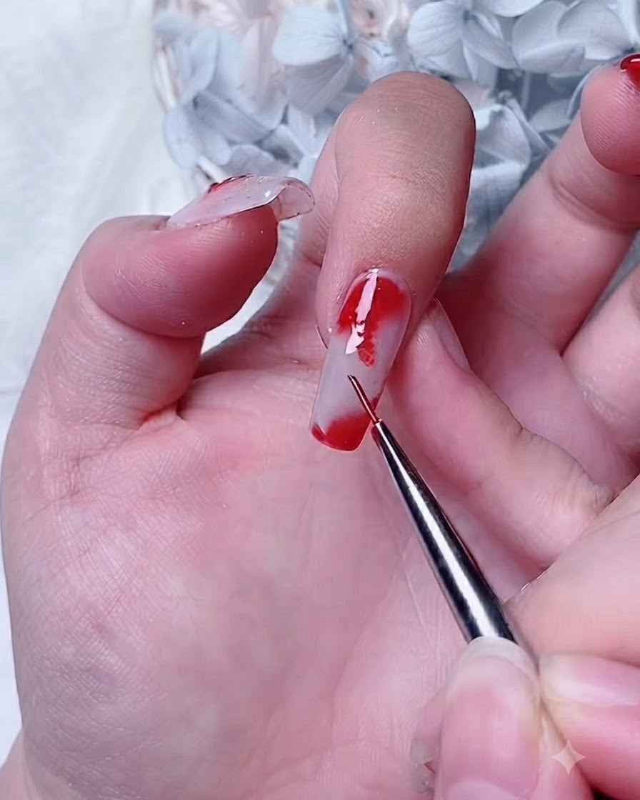 Un pinceau de détail appliquant du gel rouge sur une couche de gel blooming au coin dun ongle dindex.