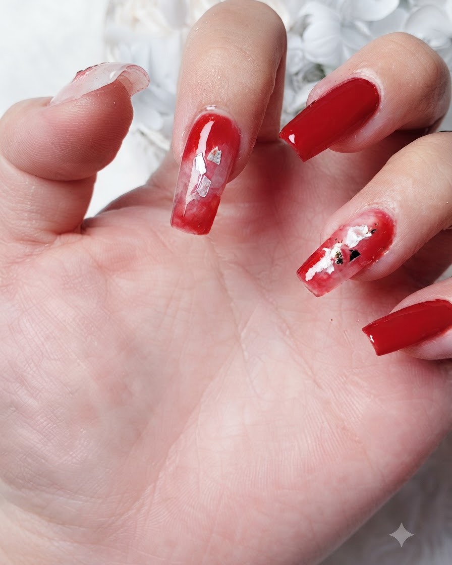 Vue rapprochée de petites pièces de feuille dor en forme de feuille placées dans une zone de gel blooming rouge diffus sur un ongle.