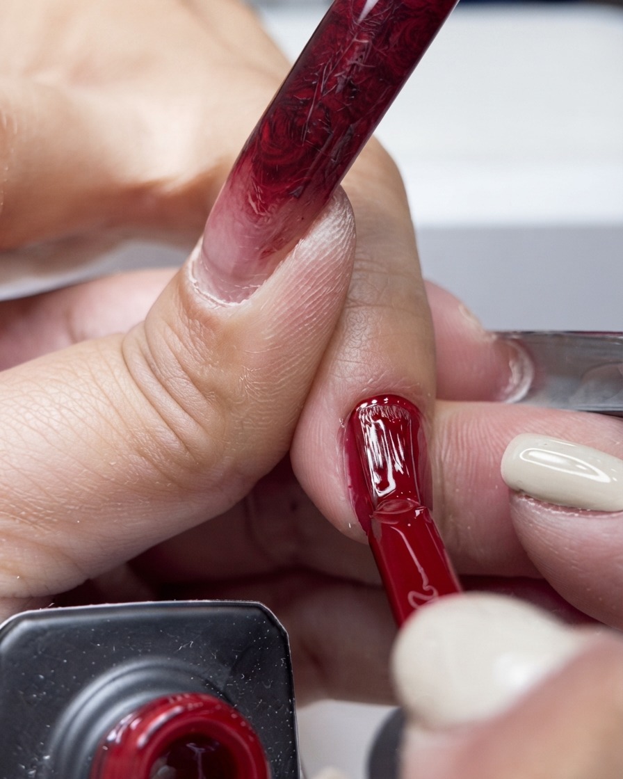 Un pinceau appliquant un vernis gel rouge vif au centre dun ongle.