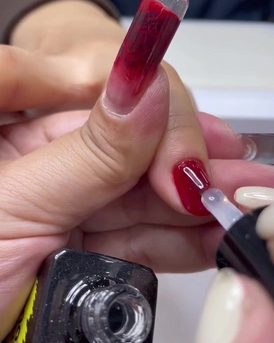 Gros plan dun pinceau à ongle appliquant un top coat transparent sur une manucure gel rouge brillante.
