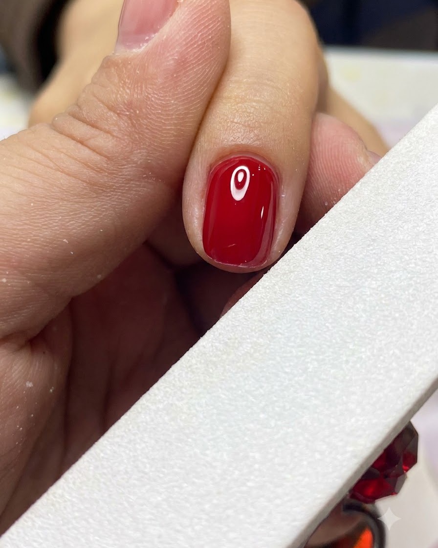 Une lime à ongles blanche modelant et lissant délicatement le bord dun ongle en gel rouge terminé.