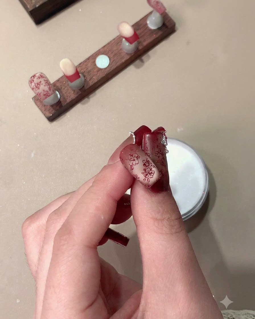 Une main tenant des faux-ongles finis présentant des motifs rouges estampés et des French tips.