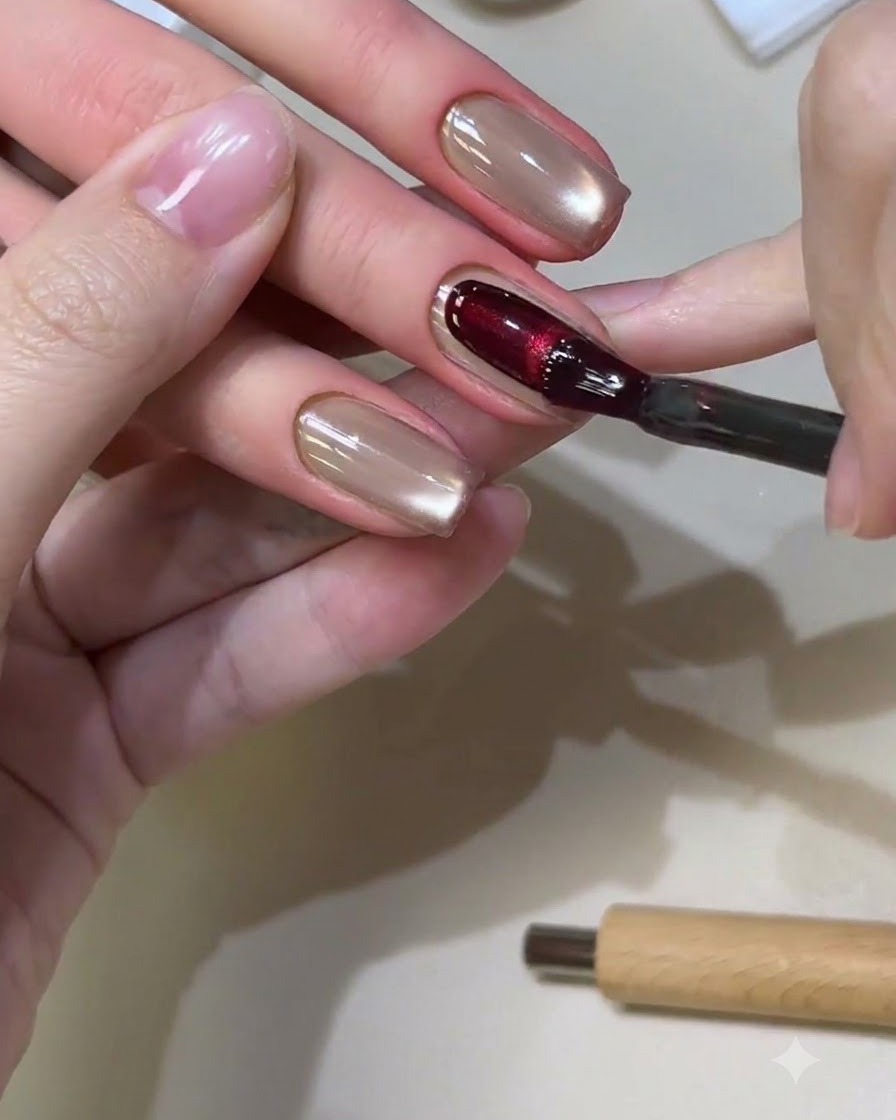 Un pinceau à ongles appliquant un gel cat-eye rouge riche sur un ongle de forme carrée.