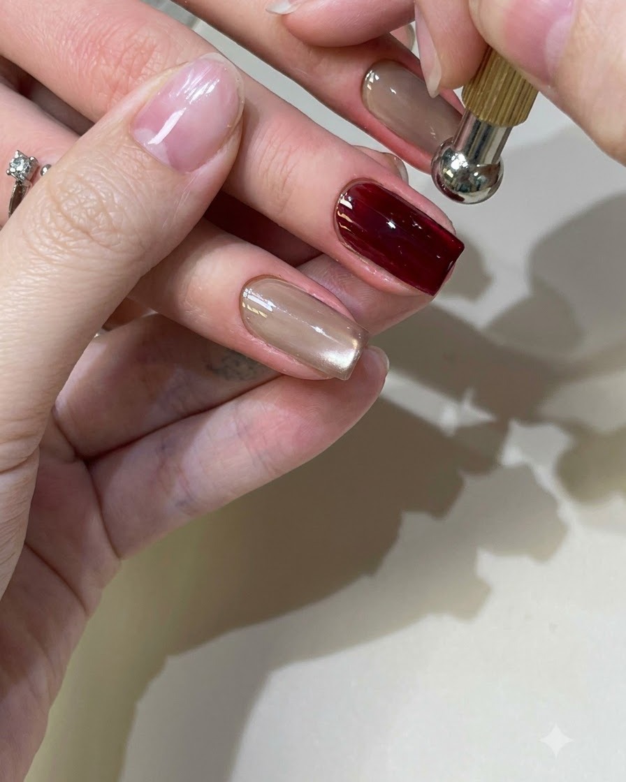 Un outil magnétique sphérique survolant un ongle en gel cat-eye rouge pour façonner le reflet lumineux.