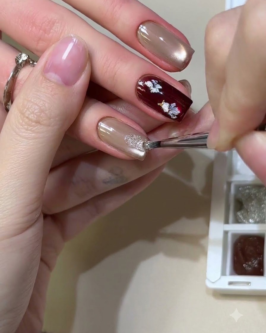 Un pinceau fin tamponnant des paillettes brillantes et réfléchissantes sur un ongle en gel cat-eye neutre.