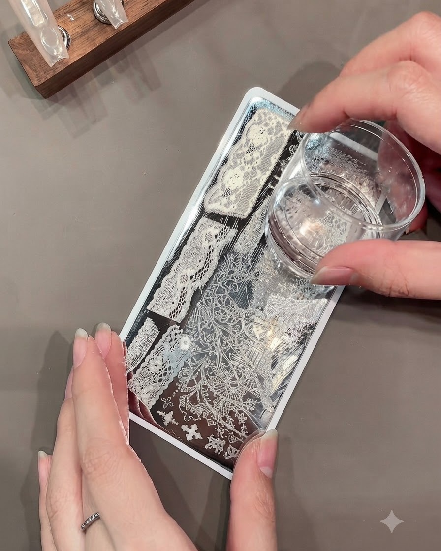 Un tampon clear jelly prélevant un motif de dentelle blanche complexe sur une plaque de stamping métallique.