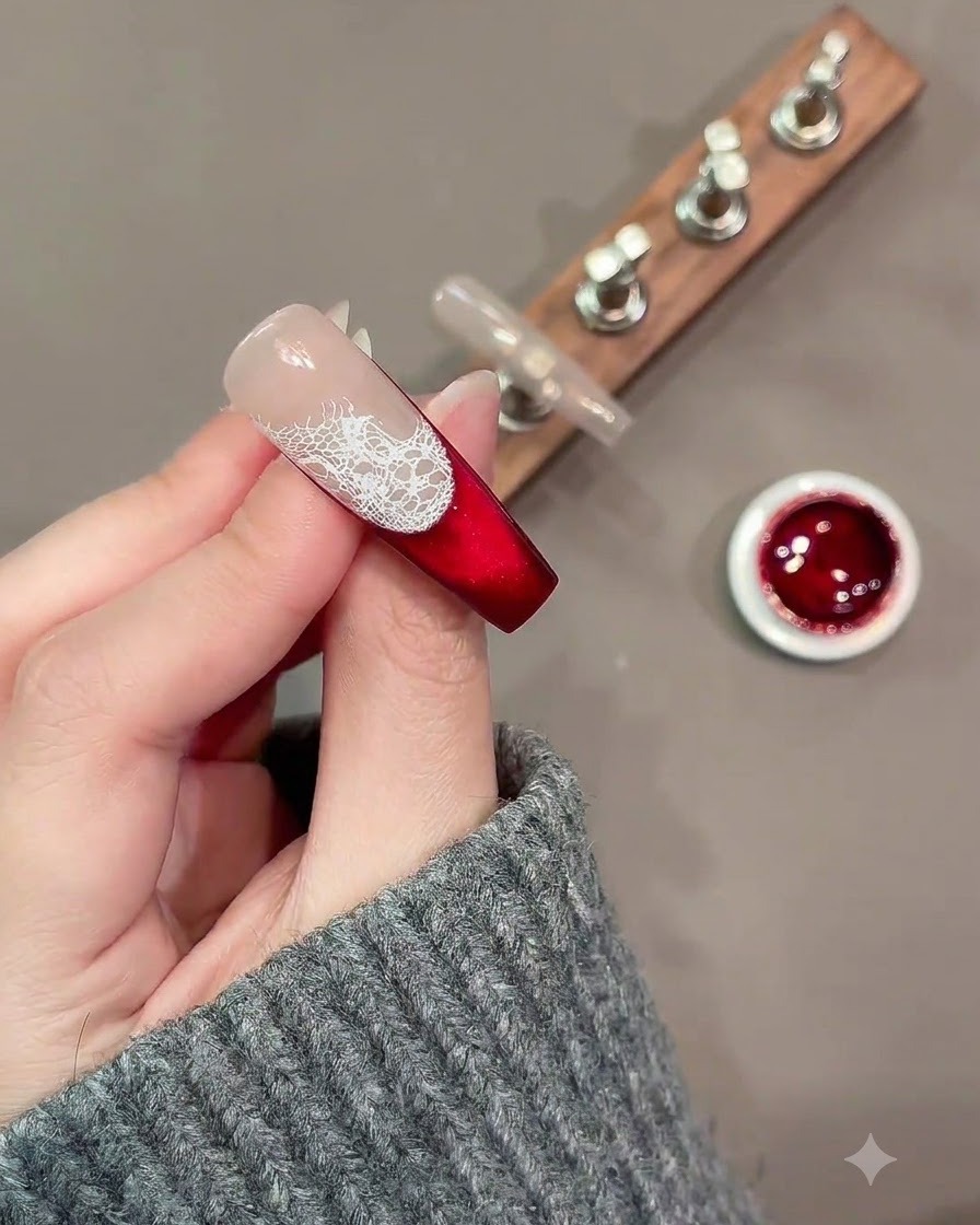 Un pinceau de nail art fin peignant des contours de roses blanches lâches sur un motif de dentelle sur un ongle rouge et nude.