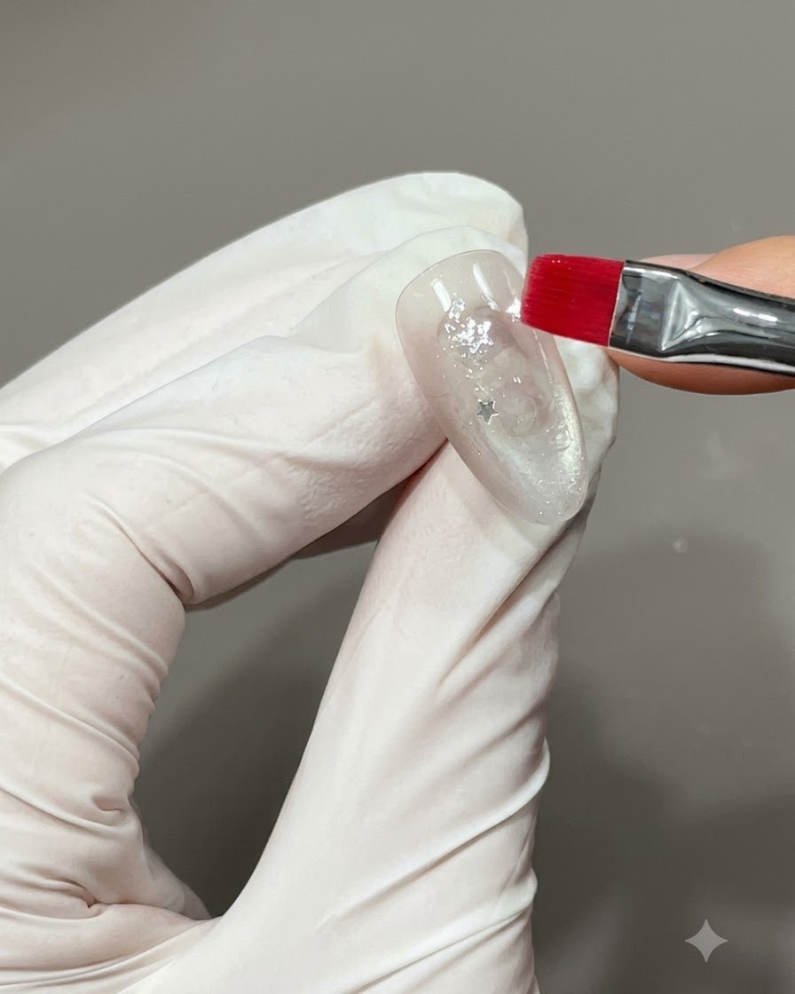 Pinceau fin posant un petit appliqué détoile métallique sur un ongle au fini scintillant.