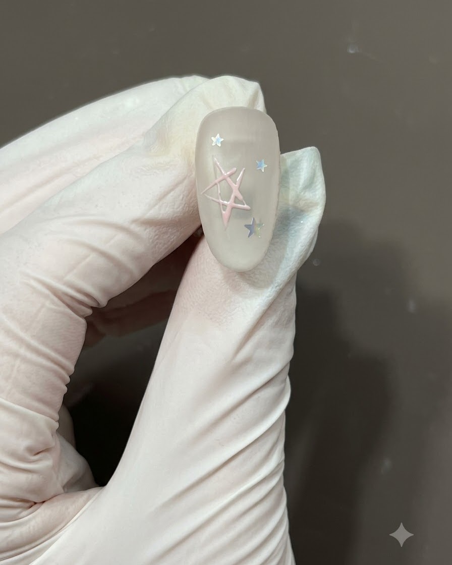 Pinceau fin de nail art remplissant le centre du contour dune étoile dessinée à la main avec du vernis gel rose clair sur un ongle mat.