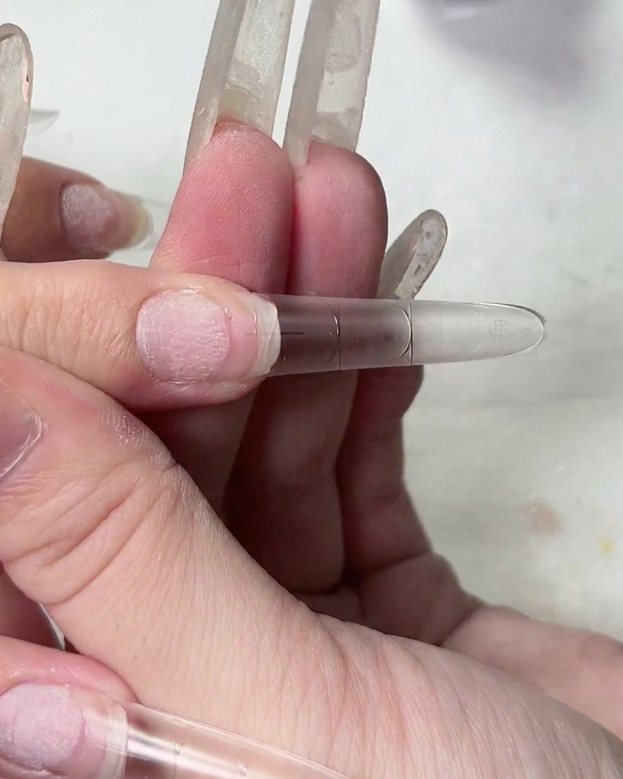 Gros plan dune main soulevant une capsule dongle, montrant la texture filandreuse du gel adhésif transparent.