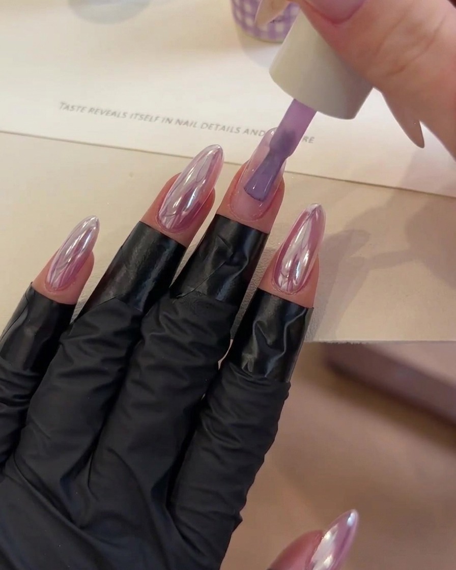 Un pinceau déposant une goutte de gel de construction transparent au centre dun ongle aux ton violet.