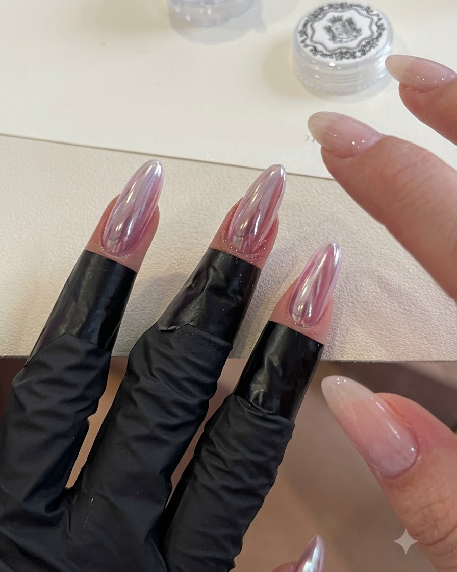 Un applicateur en mousse estompant la poudre irisée sky mirror sur des ongles chromés en forme damande.
