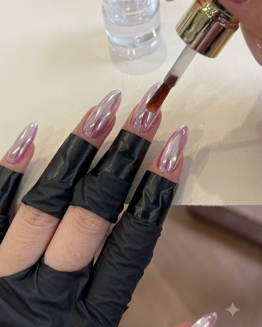 Un pinceau appliquant un top coat transparent sur des ongles brillants à finition chromée.
