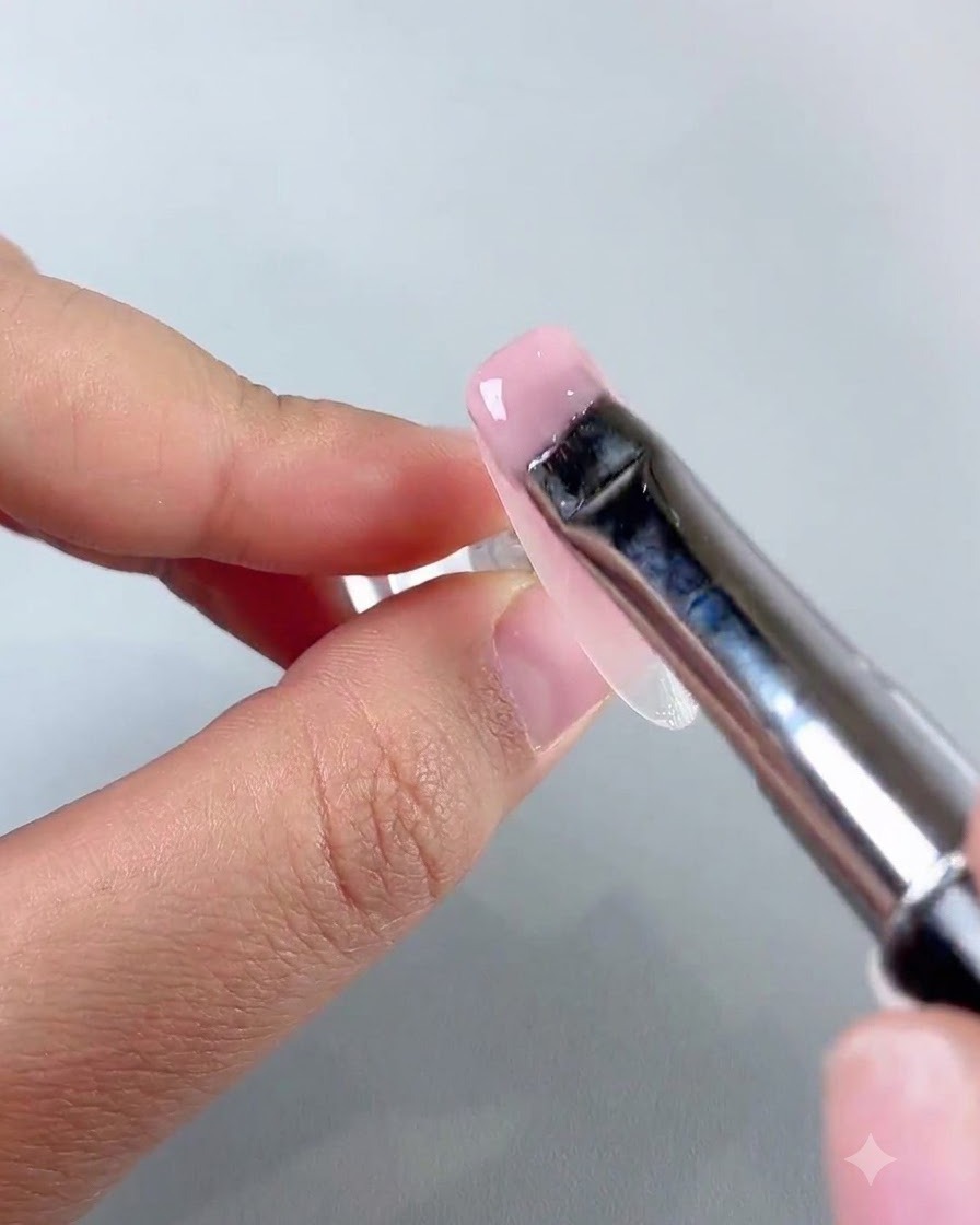 Un pinceau plat pour nail art étalant une couche lisse de gel de base jade rose clair sur la surface de longle.