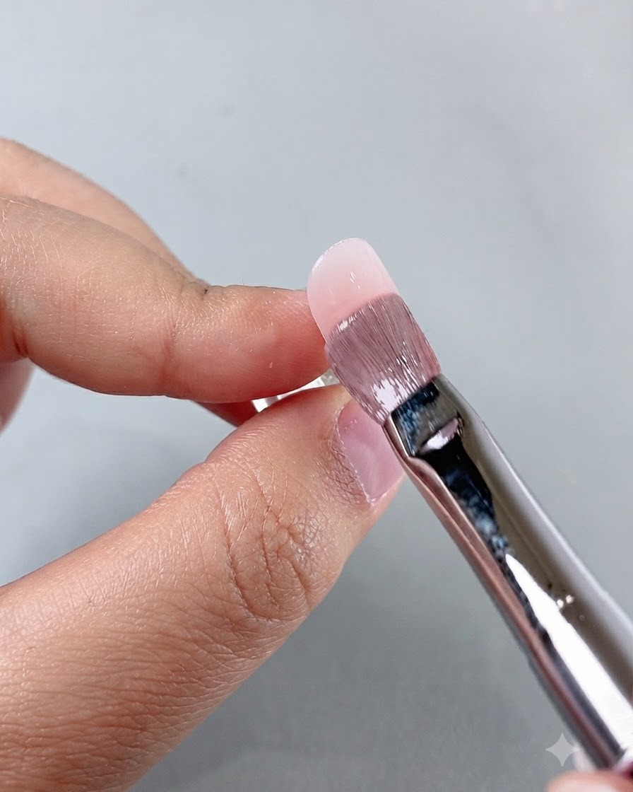 Un pinceau de manucure lissant le produit près de la zone des cuticules lors du travail sur longle.